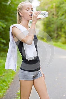 Young female runner drinking water after workout