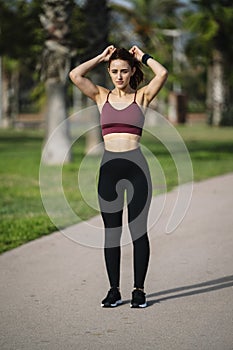 Young female runner getting ready to run morning cardio exercise. Woman athlete tying her hair in a ponytail before