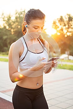 Young female runner is having break and listening to music during the run on a quay in city.