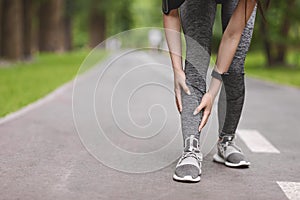 Young female runner suffering from shin splints while jogging in park