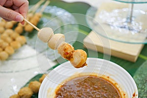 Young female`s hand holding pork meat ball stick with Thai sauce style on it