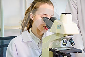 Young female scientist and chemist looking through microscope to conduct research chemistry in laboratory,concept test sample