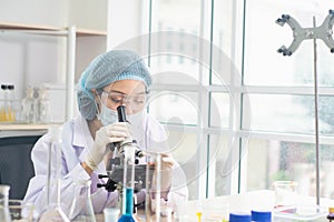 Young female scientist in protective glasses and gloves,use microscope to conduct research in laboratory,concept test sample