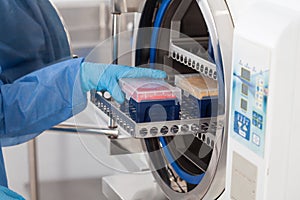 Young female scientist sterilizing laboratory material in autoclave