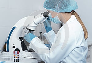 Young female scientist studying new substance or virus in microscope