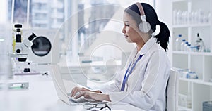 Young female scientist working on laptop with wireless headphones to do research in a modern laboratory. Medical