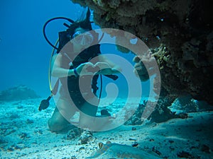 Young female on the seafloor showing love signal to a small slop