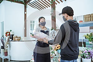 young female shopkeeper wearing a face mask and apron. servicing male flannel flower buyers