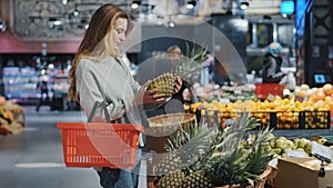 Young female shopper chooses ripe juicy healthy fruits in grocery store near counter for healthy lifestyle. Caucasian