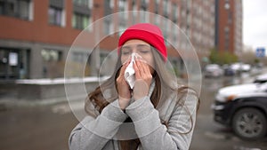 Young female sick woman, girl blowing nose to paper napkin and sneezing at street outside, healthcare, flu, people