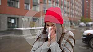 Young female sick woman, girl blowing nose to paper napkin and sneezing at street outside, healthcare, flu, people