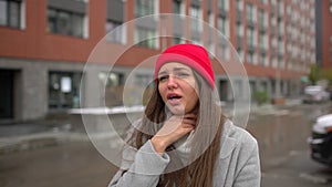Young female sick woman, girl with sore throat pain and nasty cough, coughing at street outside, healthcare, flu, people