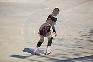 Young female skating in a outdoor skatepark in summer. Athletic person roller blading in a concrete urban park