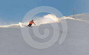 A young female skier in an orange jacket turns carving arches on the slope. A beautiful sunny day in the mountains, on the ski