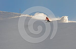 A young female skier in an orange jacket turns carving arches on the slope. A beautiful sunny day in the mountains, on the ski