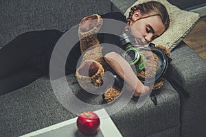 Young Female Sleeping On Sofa WIth Toy Bear Wearing Gas Mask