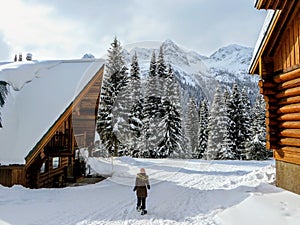 A young female snowshoer walking in between two wood cabins during the winter in the remote snow covered forests of Fernie