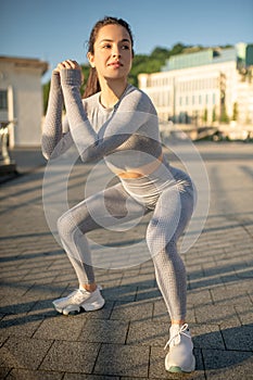 Young female sportsperson in grey sportswear doing squats