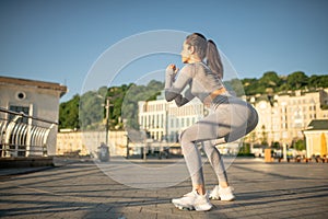 Young female sportsperson in grey sportswear doing squats