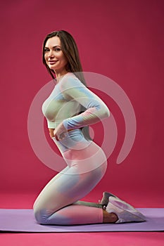 Young female in sportswear, kneeling on mat, during workout.