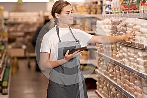 Young female staff using digital tablet in supermarket.