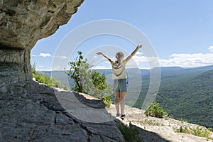 Young female stand on rock on peak in high mountains with hands up expressing feeling og freedom and happyness.