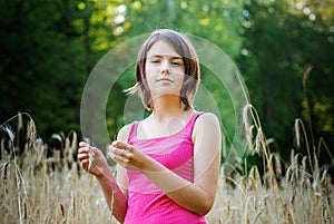 Young female stands in crop field holding flower