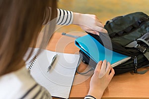 Young female student behind her desk at class, taking out her textbooks.