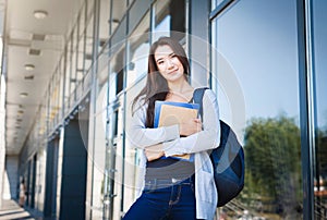 Young female IT student, with books and backpack. Staying outside before lesson and smiling