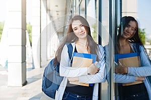 Young female IT student, with books, smartphone and backpack. Staying outside before lesson and smiling