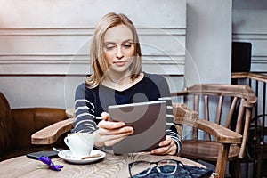 Young female student is chatting on digital tablet with friend while sitting in cafe, attractive woman using laptop