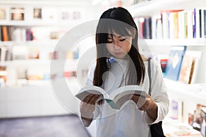Young female student choosing new books on shelves