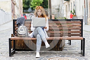 Young female student concentrated on her studying using laptop on the bench at the street
