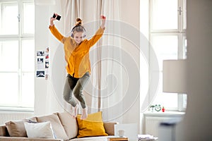 A young female student with headphones jumping on sofa when studying.