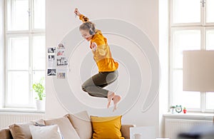 A young female student with headphones jumping on sofa when studying.