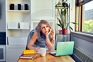 young female student with laptop and cup of coffee studying at home