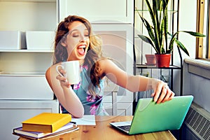 young female student with laptop and cup of coffee studying at home
