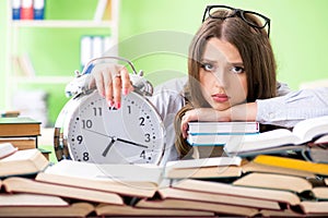 Young female student preparing for exams with many books in time
