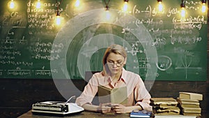 Young female student read book in front of the chalkboard. Portrait of young teacher reading book by blackboard in the