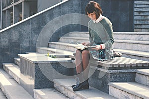 Young female student is  reads book on stairs.