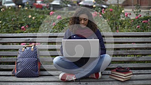Young female student sitting on bench outdoors full-absorbed in the study
