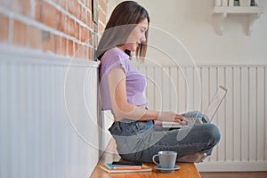 Young female student sitting comfortably is using a laptop to make video calls with friends at home