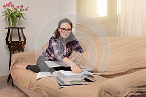 A young female student sitting at the couch, using books