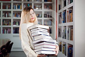 Young female student study in the school library with a many books in her hands.