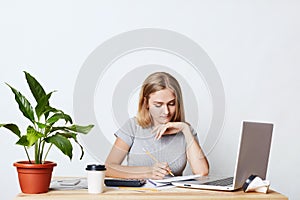 Young female student studying math, preparing report, making notes from laptop, writing in her copy book, isolated over white back