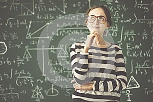 Young female student thinking in front of classroom board