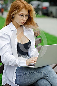 Young female student using her laptop sitting on the bench in park