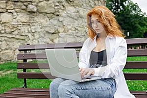 Young female student using her laptop sitting on the bench in park