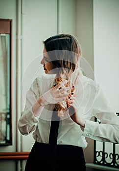 A young female student wearing a uniform and a black tie is seen combing her blonde hair. Youth, education, and professionalism.