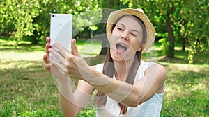 Young female student in white shirt sitting on grass on college campus doing selfie on mobile phone